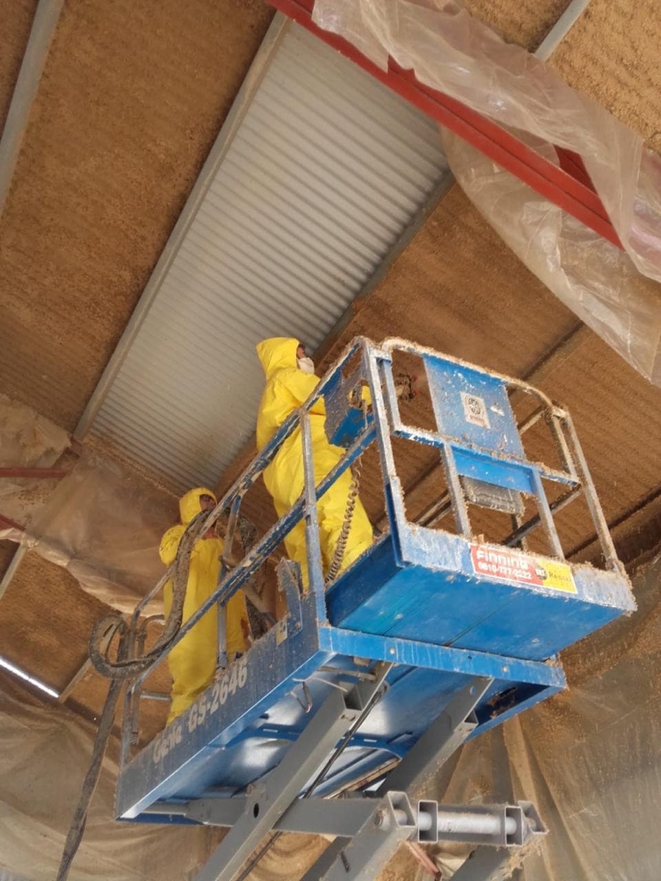 Aplicación de celulosa proyectada en techo de galpón industrial con plataforma elevadora