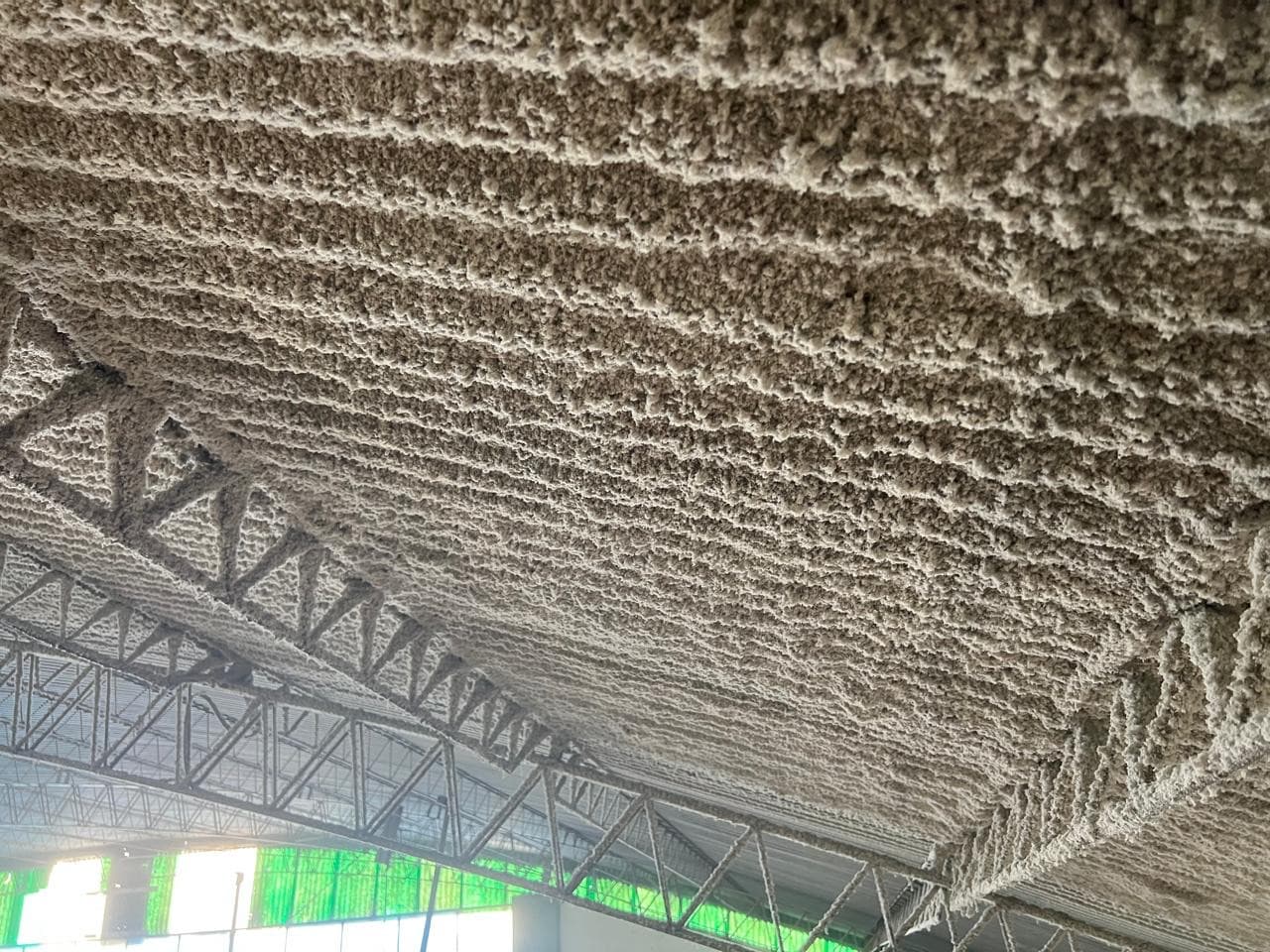 Detalle de la celulosa proyectada terminada sobre la estructura curva del techo del gimnasio